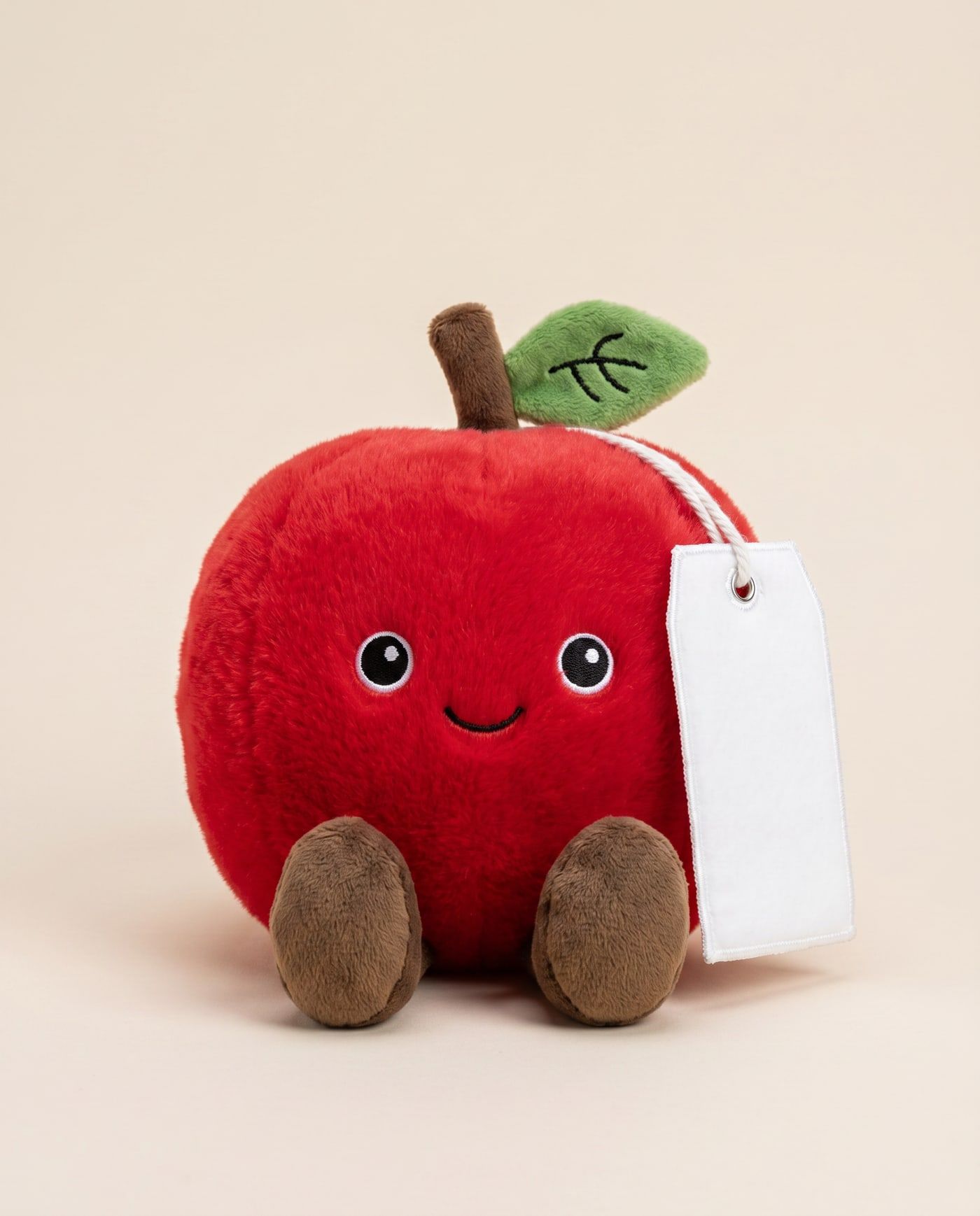 Archie the Apple TagTales plush sitting down, showing the blank white fleece personalisation tag