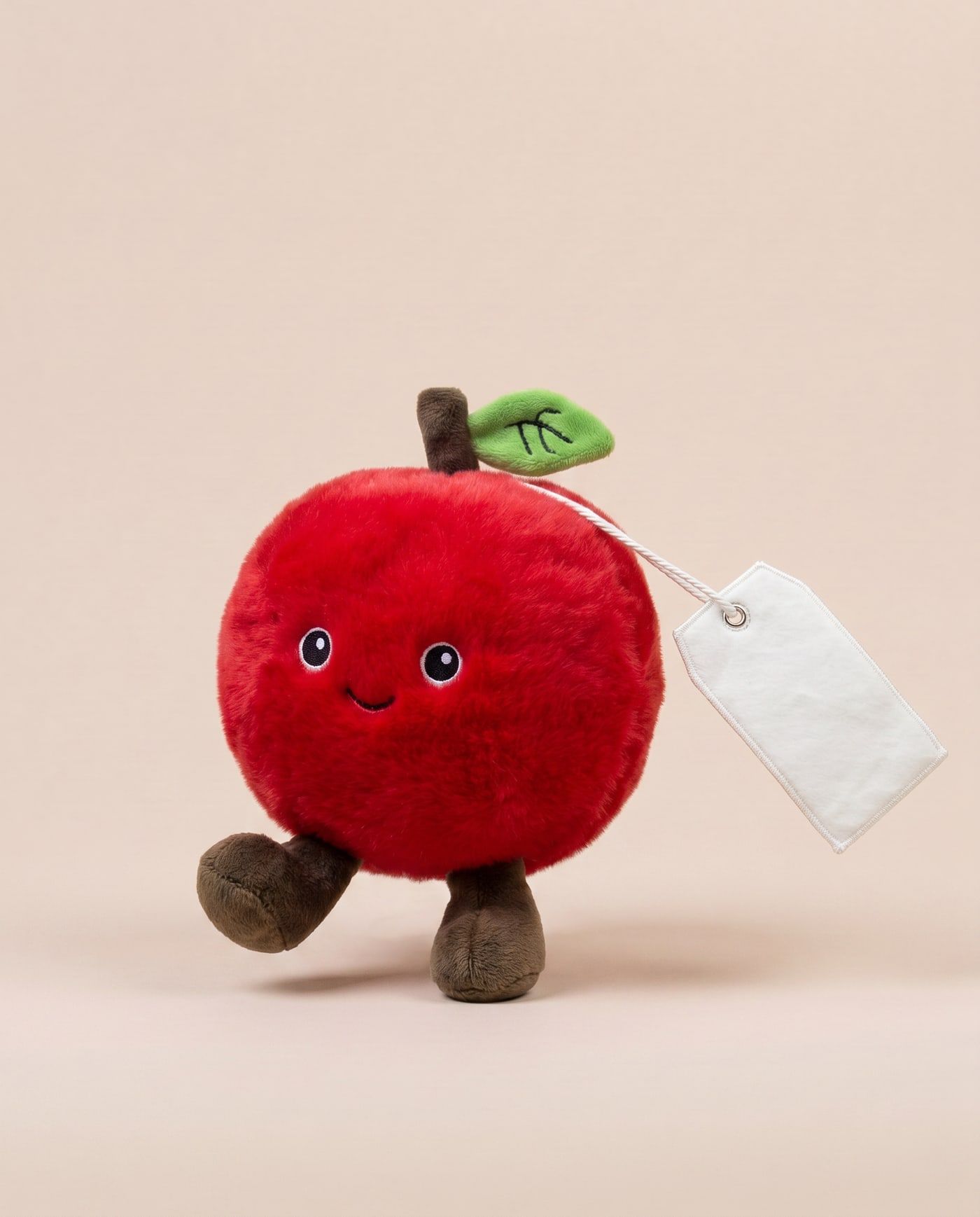 Archie the Apple TagTales plush standing on a cream background, with the blank white fleece personalisation tag hanging from a cord