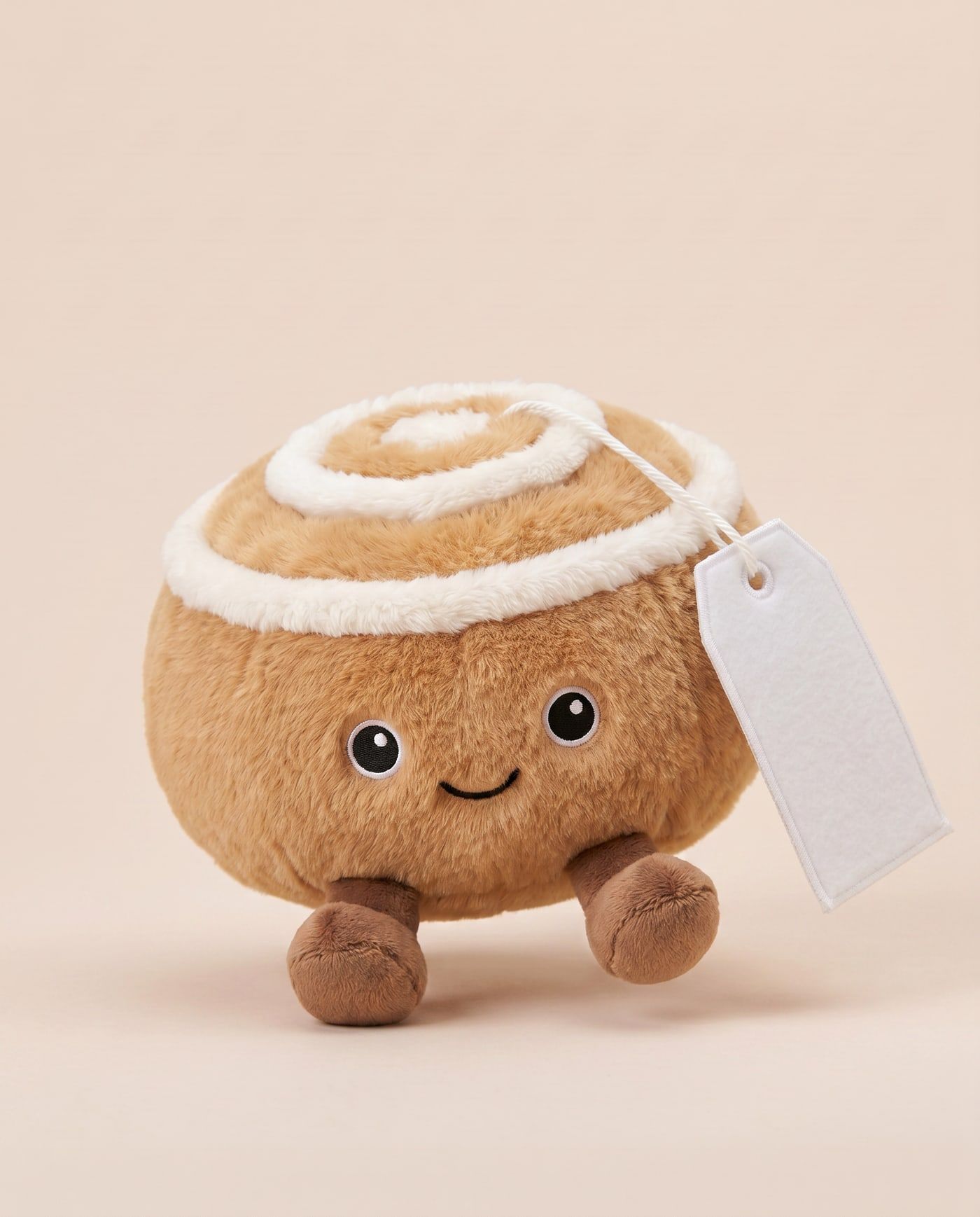 Cindy the Cinnamon Bun TagTales plush standing on a cream background, with the blank white fleece personalisation tag hanging from a cord