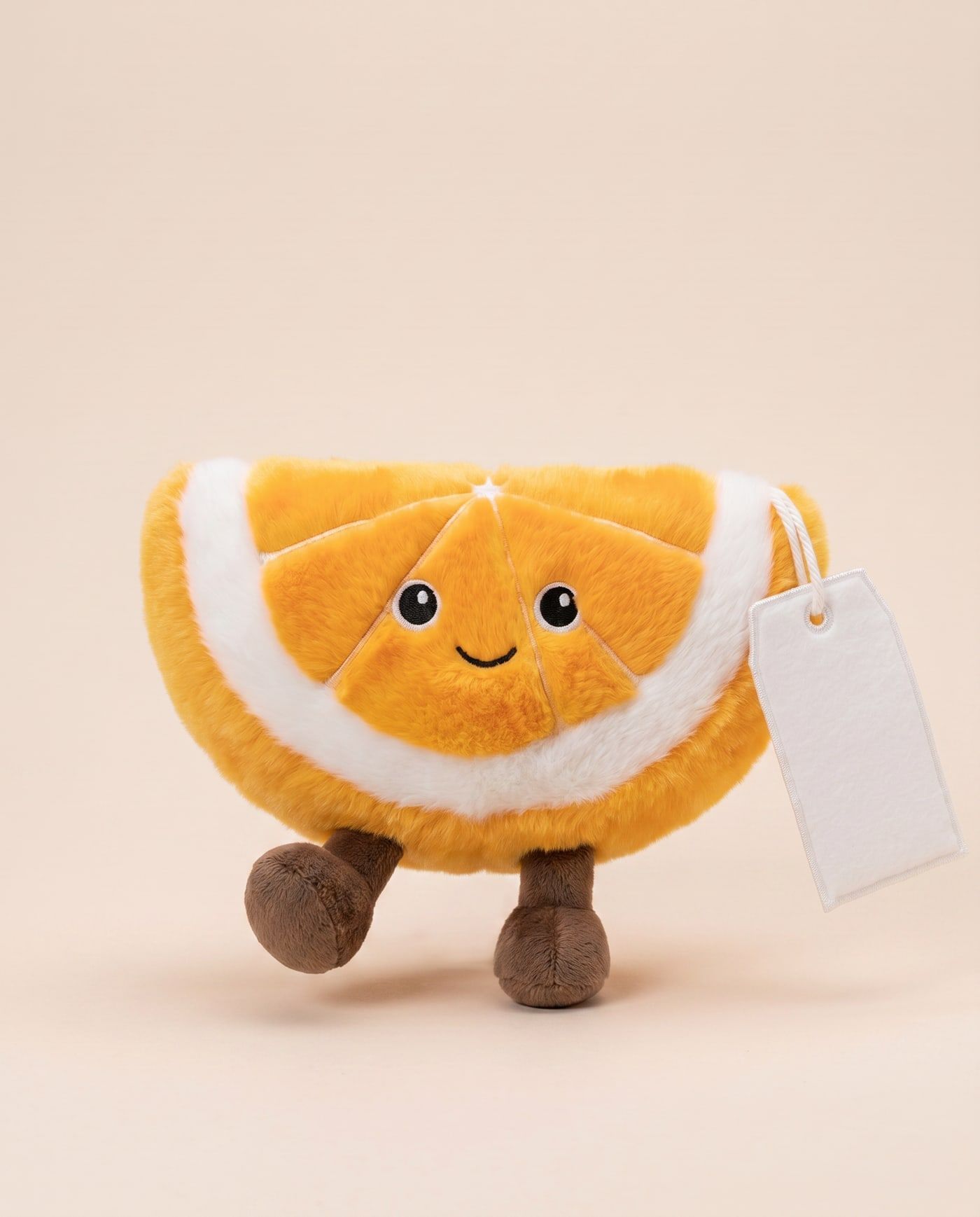 Ollie the Orange Slice TagTales plush standing on a cream background, with the blank white fleece personalisation tag hanging from a cord